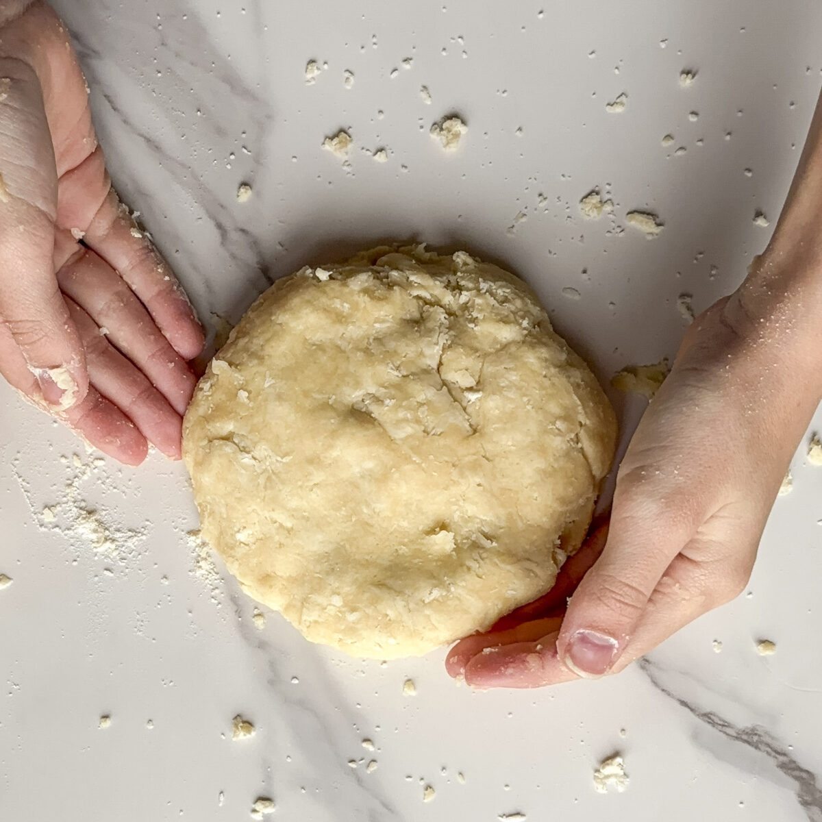 Pie dough on a table and two hands around the dough