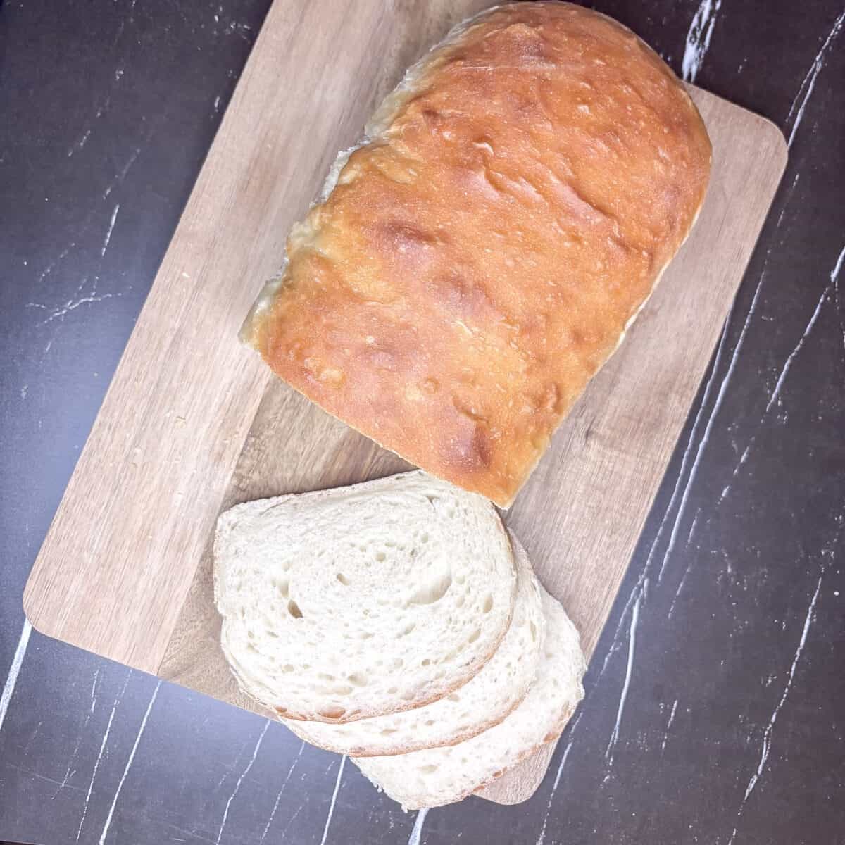 a loaf of bread on a wood cutting board slices with 3 slices on the board. 
